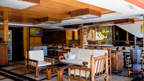 A lobby with wooden furniture, a large TV screen, and a ship model. - Safari Natal Beach Hotel (Natal)