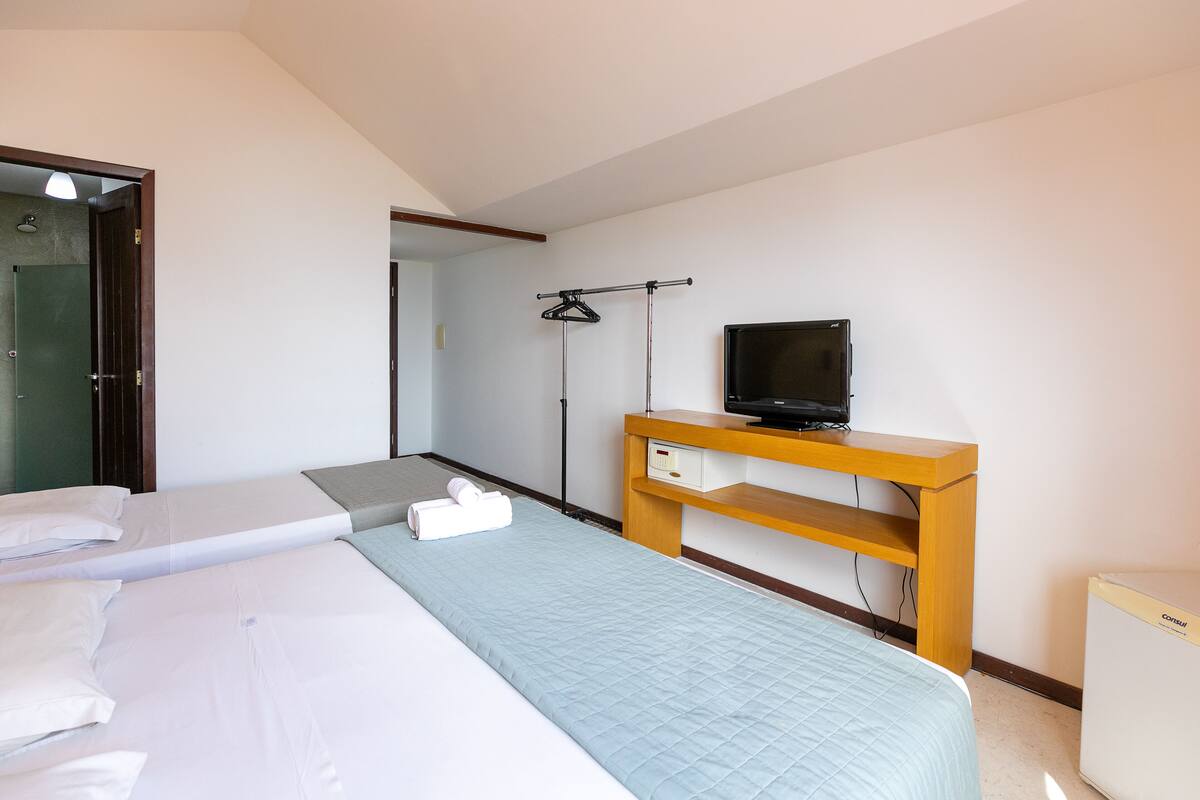 A hotel room with two beds, a TV on a wooden stand, and a small refrigerator.