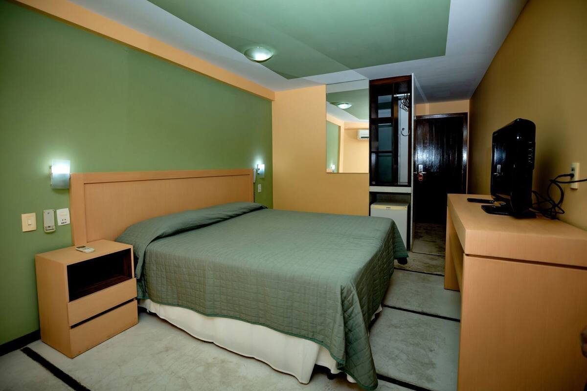 A bedroom with a bed, nightstand, dresser, and a mirror.