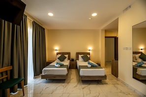 A hotel room with two beds, a chair, a mirror, and a door leading to another room.