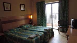 A hotel room with two beds, a TV, a chair, and a balcony with curtains. - Euro Club Hotel (St. Paul's Bay)