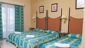 A hotel room with two beds, each with a patterned bedspread and a white towel. There are two bedside tables with lamps, and the room has a beige wall with framed pictures. - Euro Club Hotel (St. Paul's Bay)