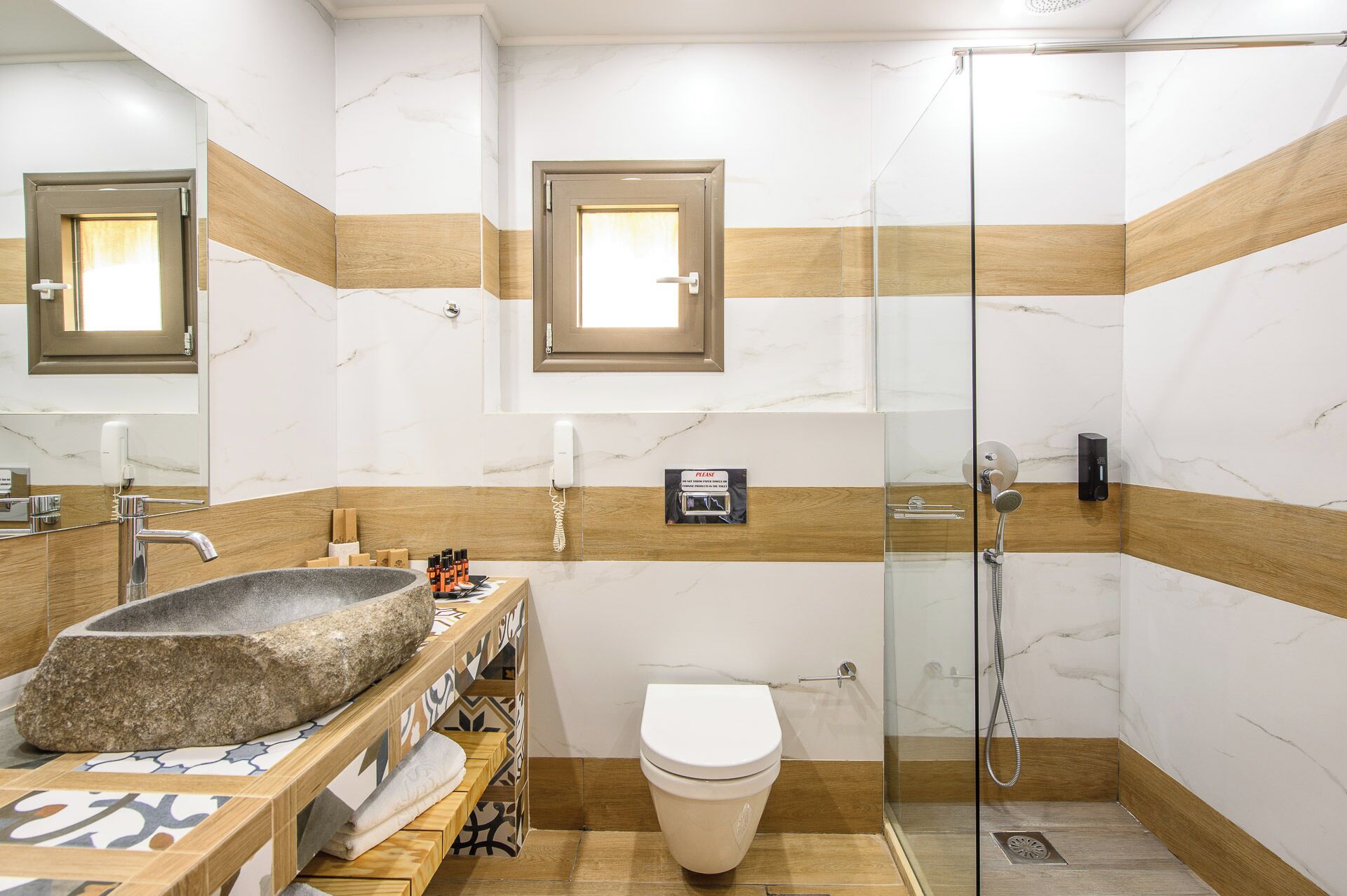 Un baño moderno con lavamanos de piedra, inodoro y ducha con mampara de vidrio.