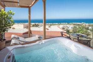 A hot tub with a view of the sea, outdoor seating, and a table with a bowl of fruit.