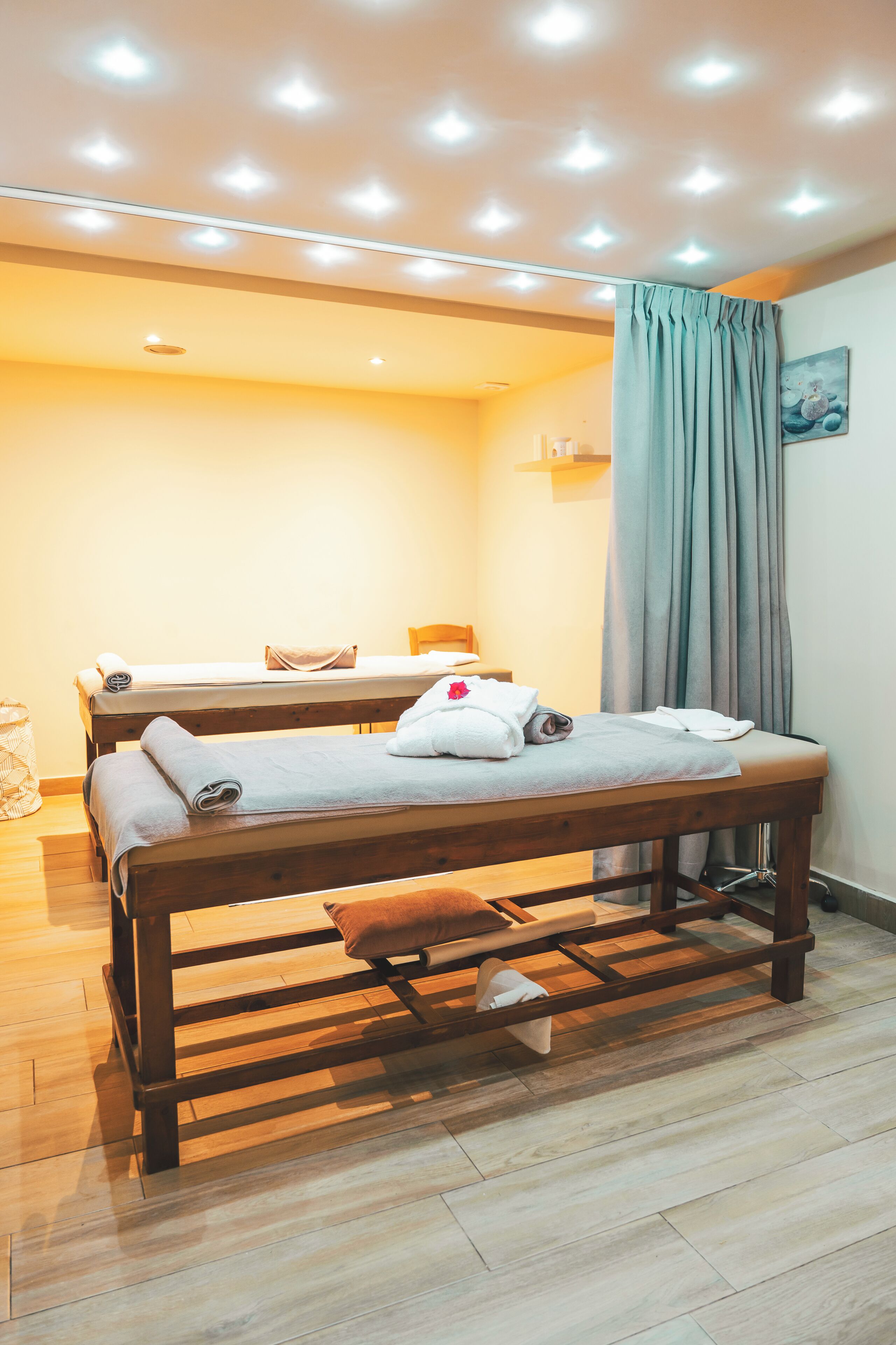 A room with two beds, wooden flooring, and a ceiling with recessed lighting.