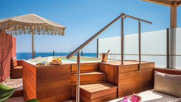 A wooden deck with a hot tub, a metal railing, and a view of the ocean.