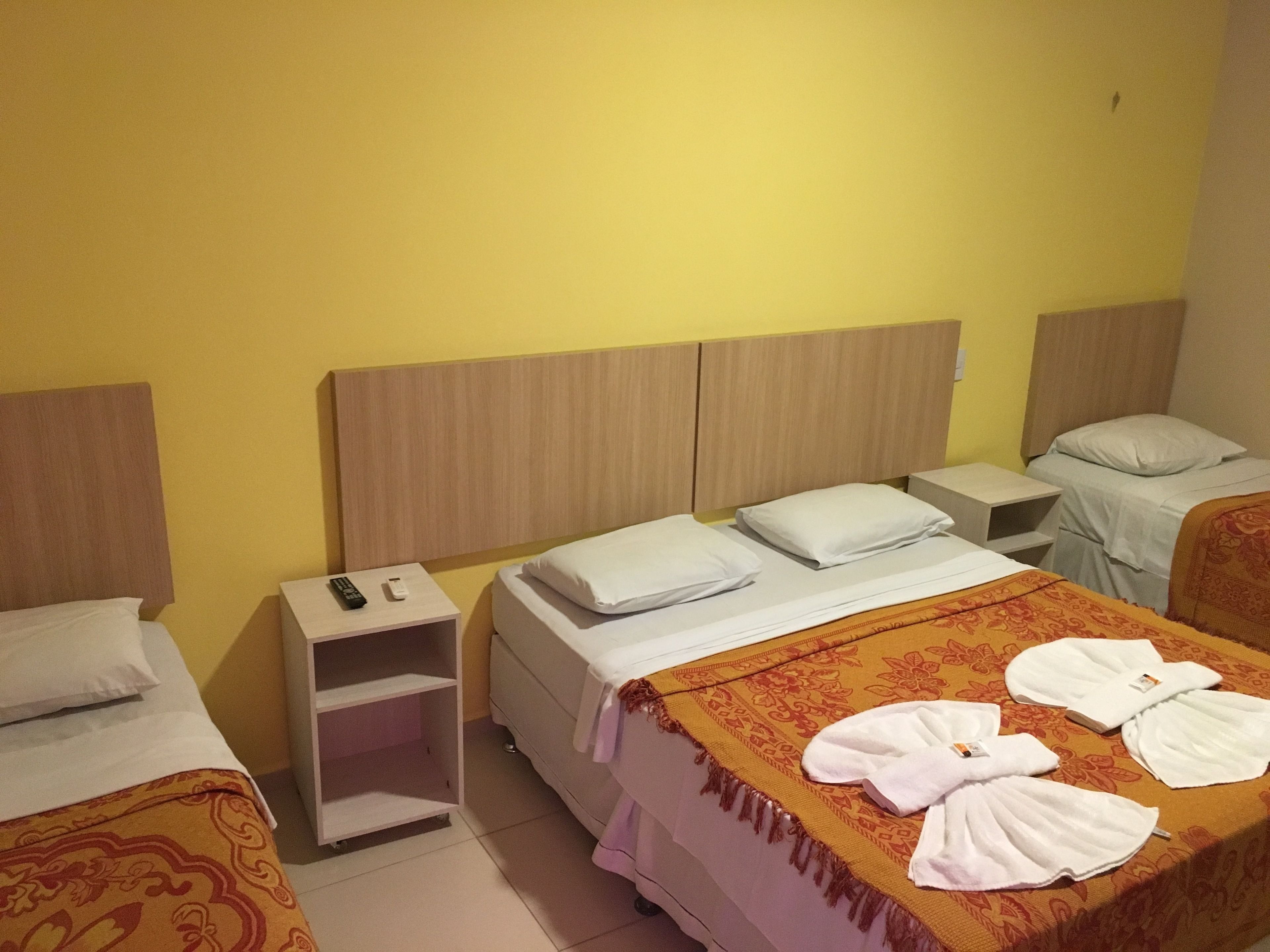 A hotel room with two single beds, a nightstand with a remote control, and a bathroom with a towel on the bed.