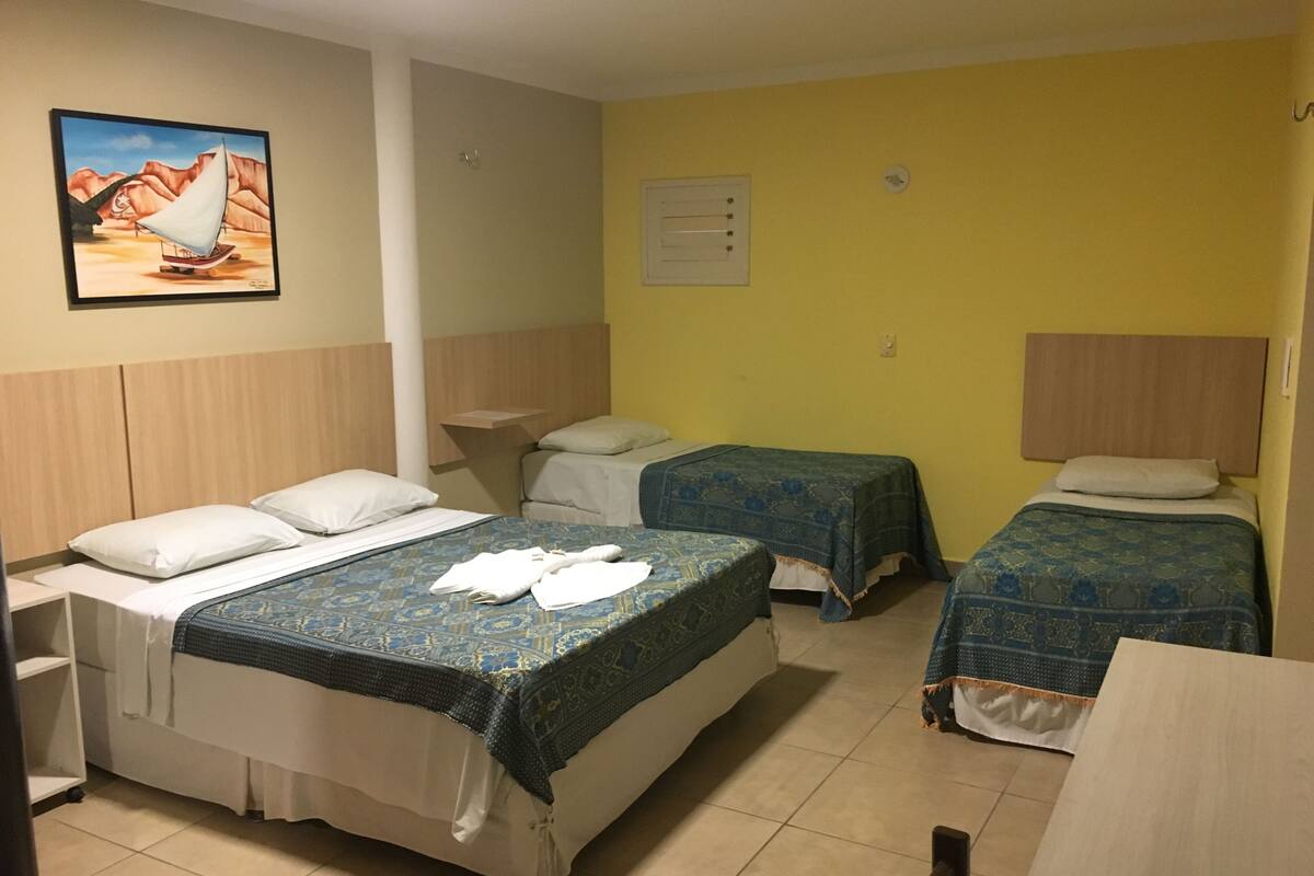 A hotel room with two beds, a small table, a chair, a painting on the wall, and a window.