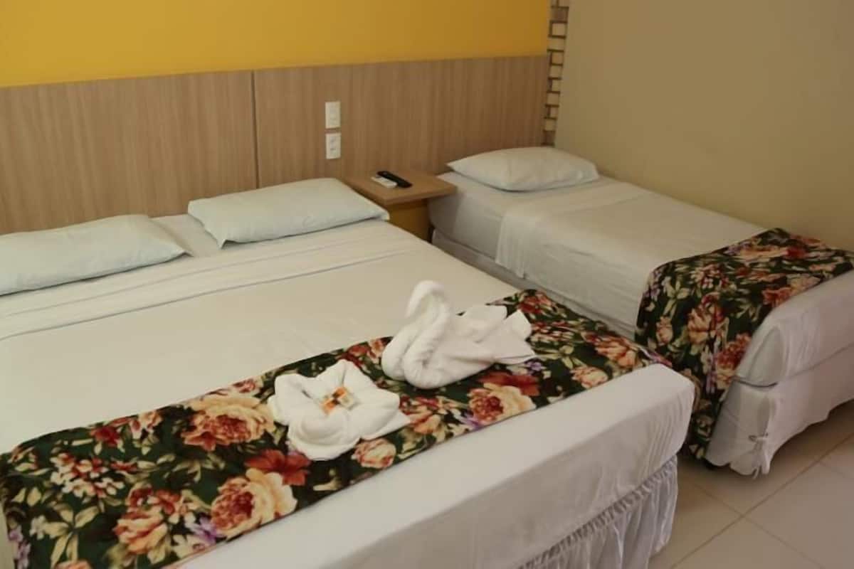 A hotel room with two single beds, a wooden headboard, a nightstand with a phone, and a floral bedspread.