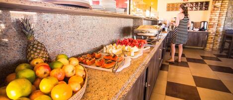 A buffet counter with a variety of fruits and vegetables, including pineapple, mangoes, and tomatoes.