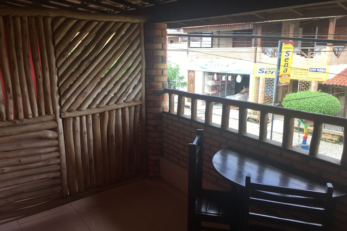 A wooden partition with diagonal slats, a brick wall, and a balcony with a table and chair.