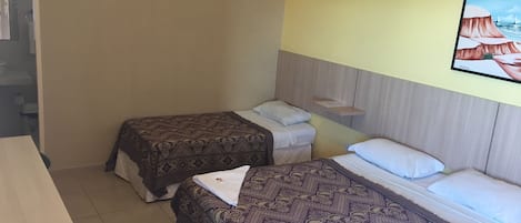 A room with two beds, a wooden headboard, a small shelf, and a painting on the wall.