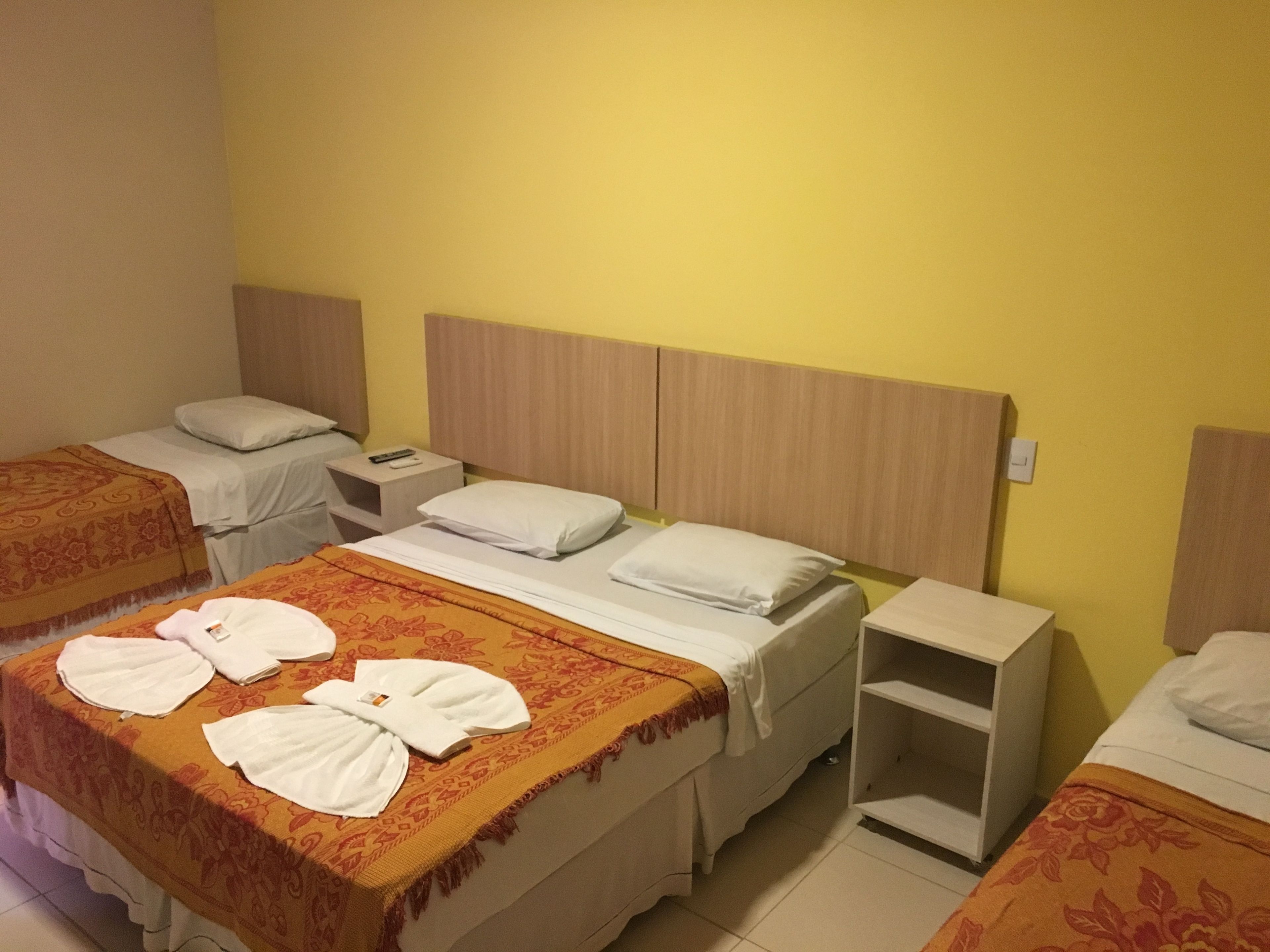 Habitación de hotel con tres camas individuales, cada una con cabecera de madera, ropa blanca y una mesita de noche con lámpara.