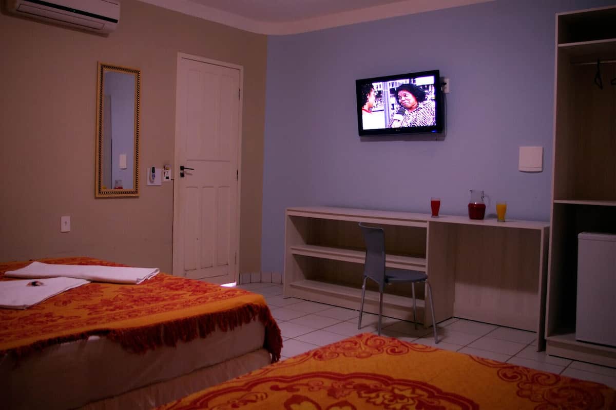 A hotel room with two beds, a TV, a desk with a chair, and a wardrobe.