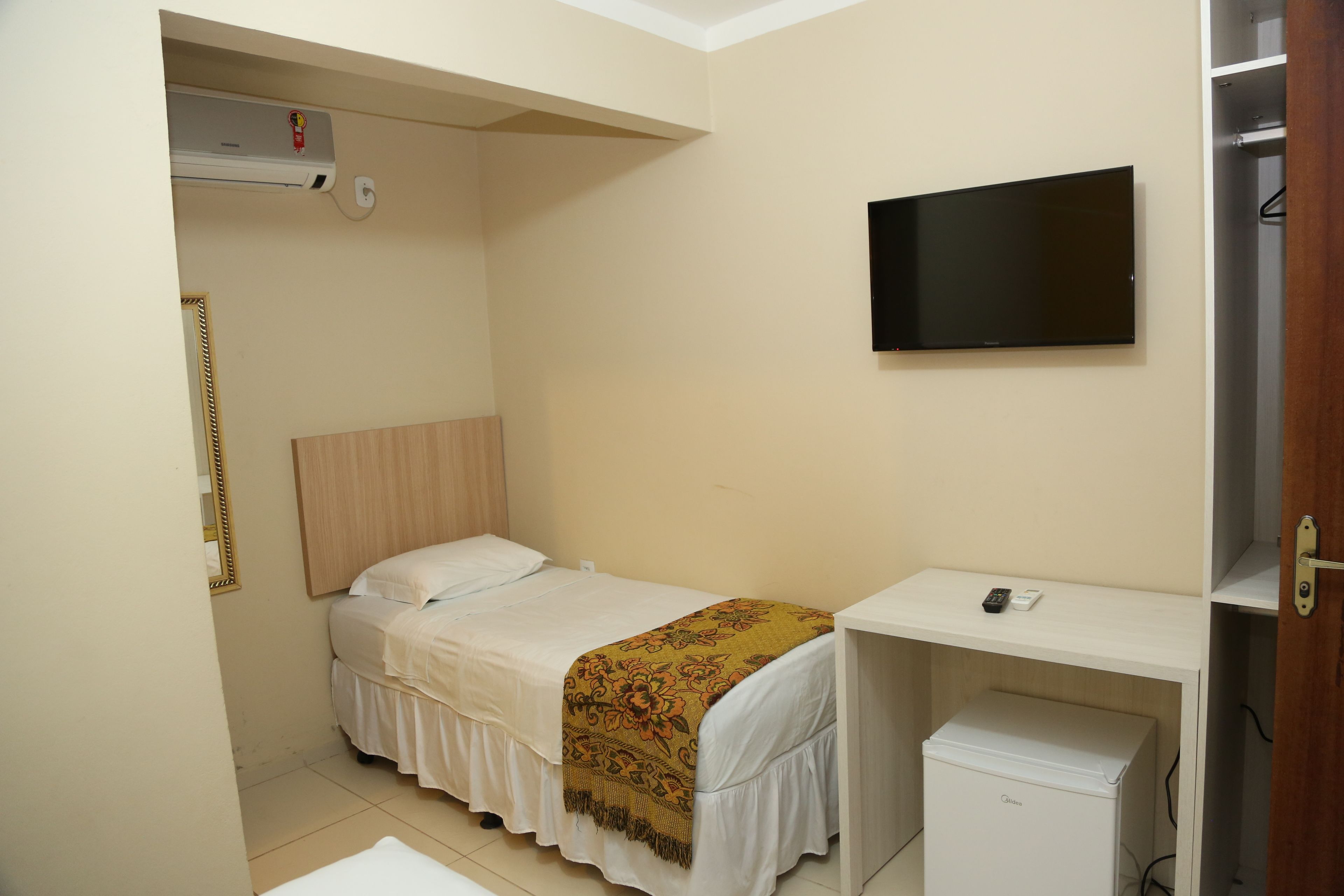 A small, neatly arranged bedroom with a bed, a desk, a television, and a wardrobe.
