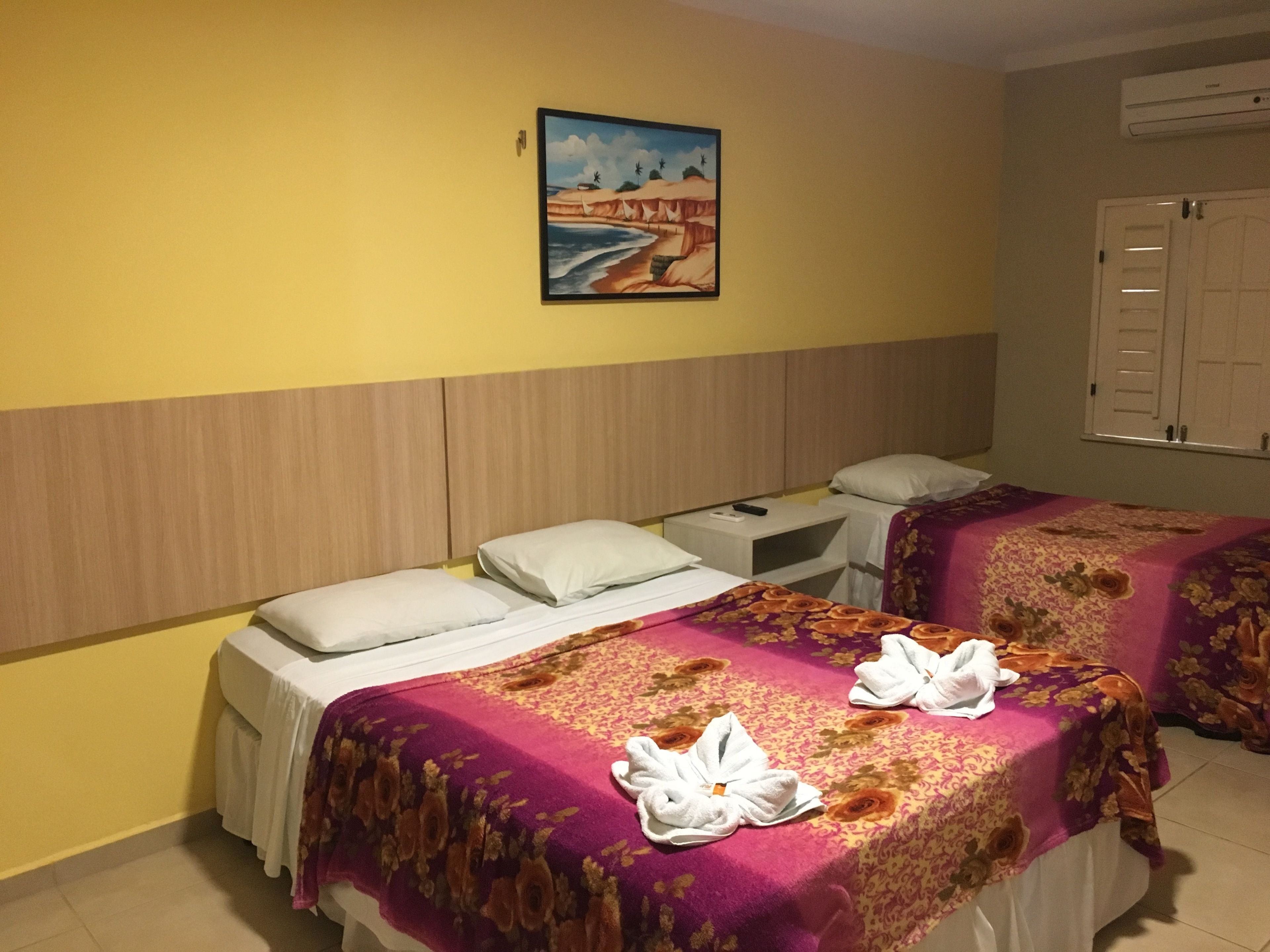 A hotel room with two beds, a painting on the wall, and an air conditioning unit.