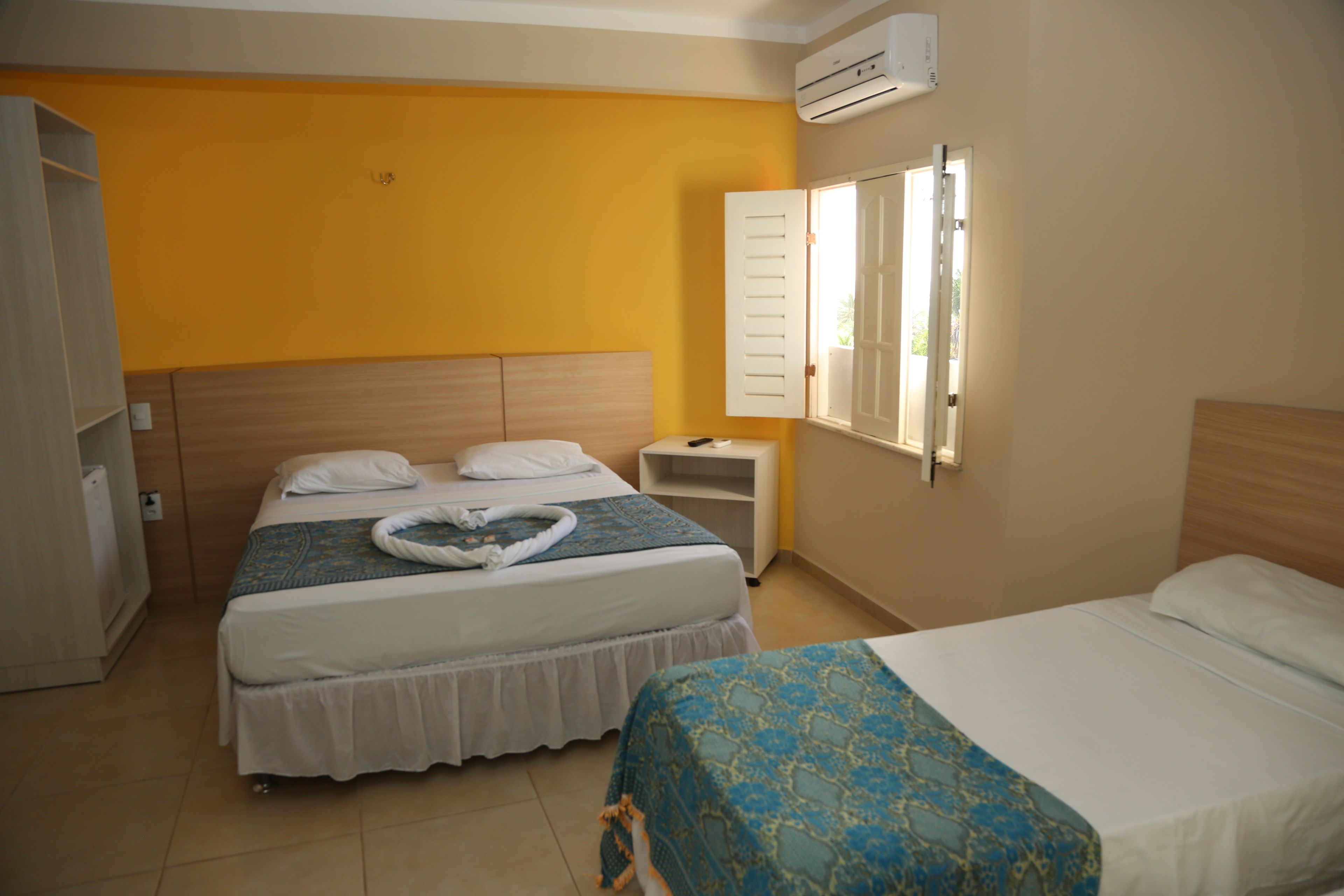 A hotel room with two beds, a small bedside table, a wardrobe, and an air conditioning unit.
