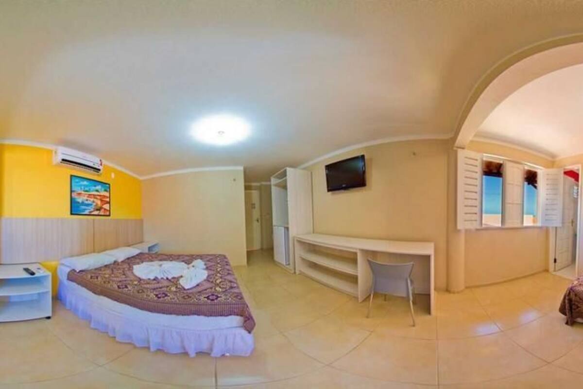 A hotel room with two beds, a TV, a desk, and a window with shutters.