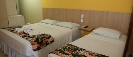 A hotel room with two beds, each with floral bedspreads and white pillows. There is a wooden headboard, a bedside table with a remote control, and a mirror on the wall.