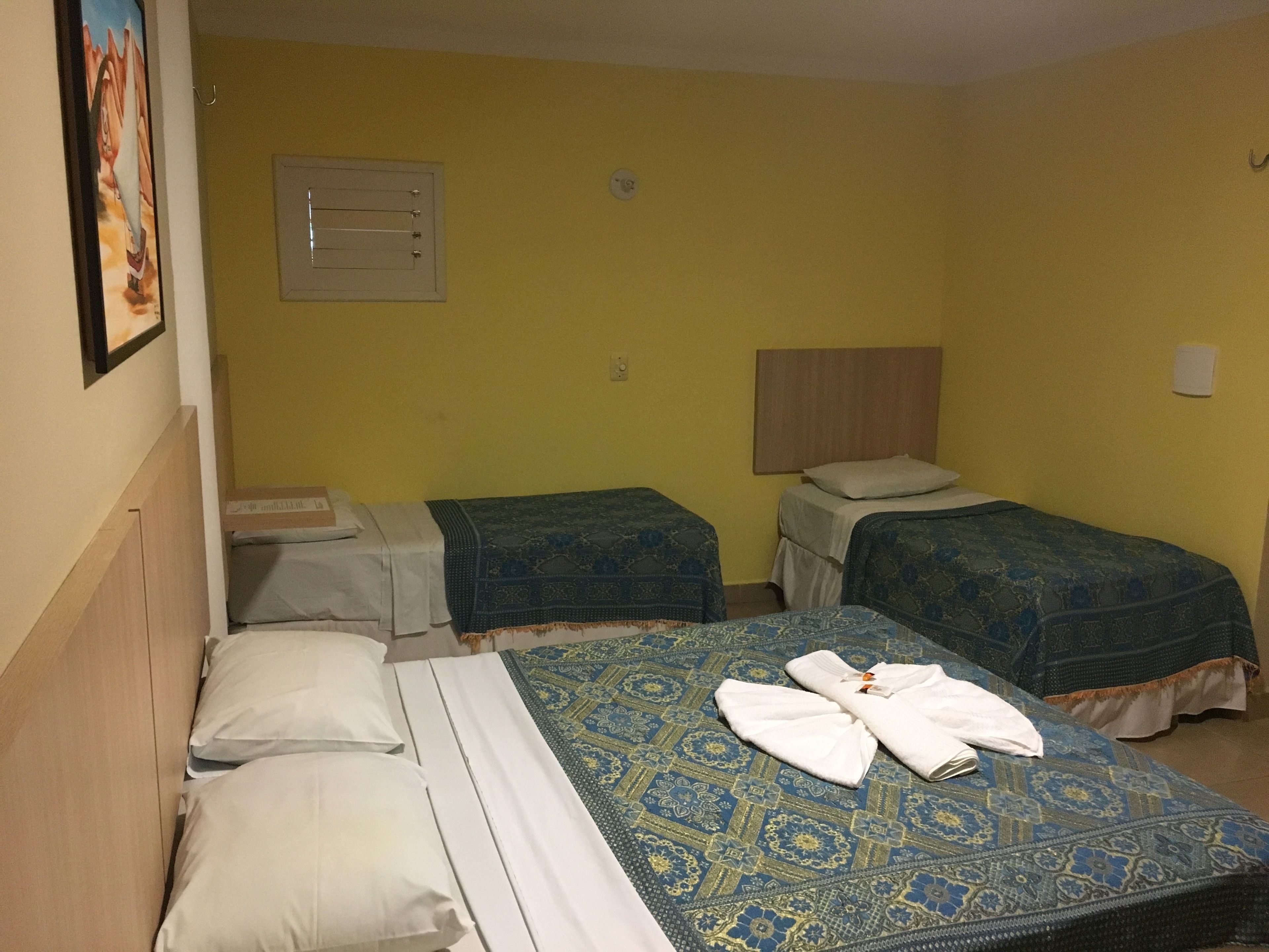 A hotel room with two single beds, a large bed, and a small table.