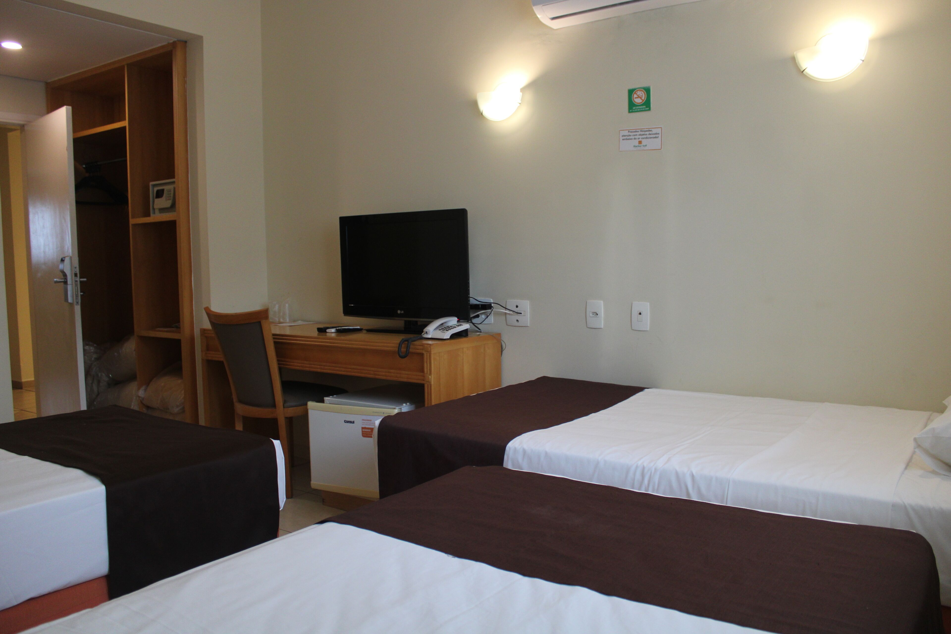 Une chambre d’hôtel avec deux lits, un bureau avec un ordinateur, une chaise et un petit réfrigérateur.