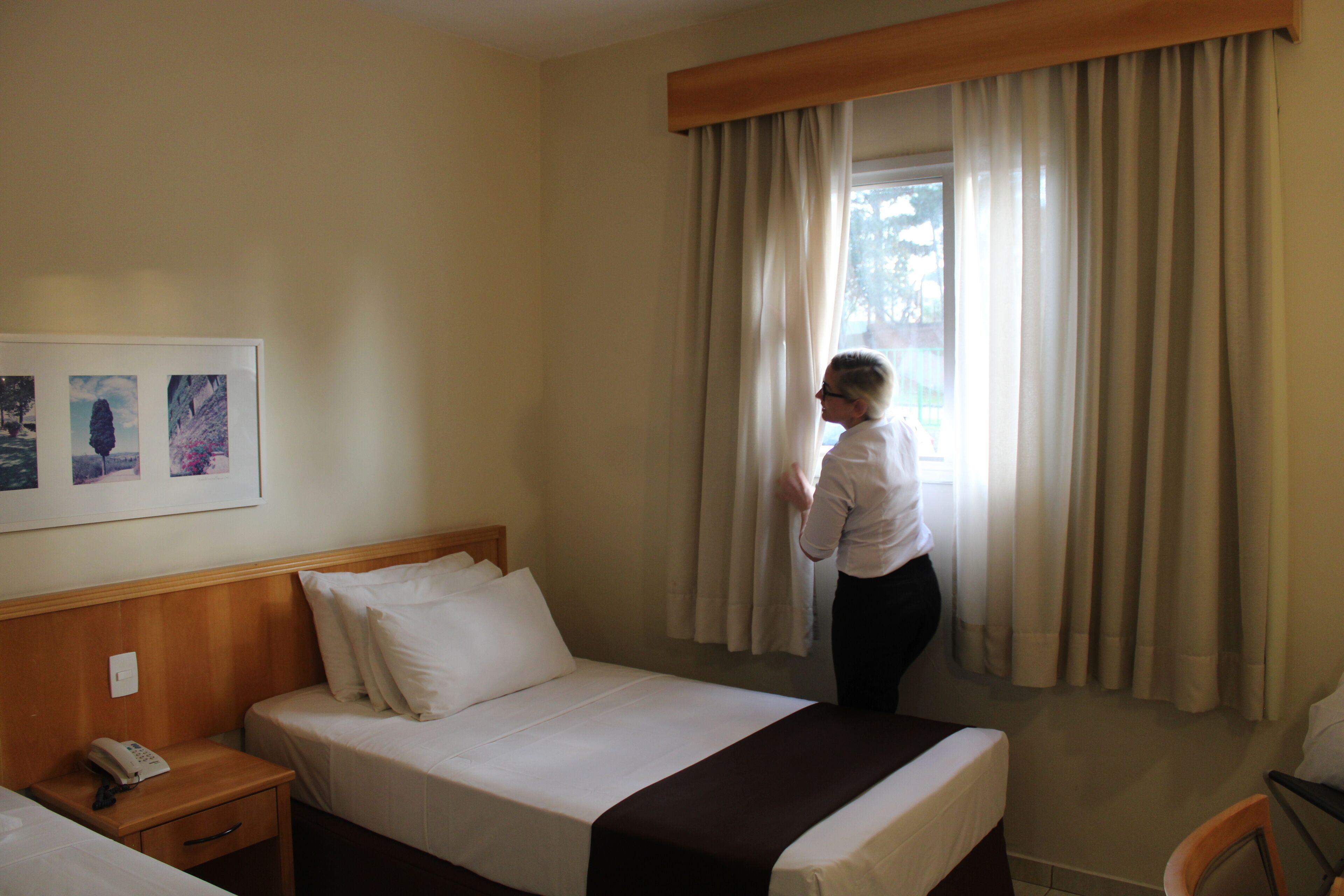 Ett hotellrum med en säng, ett nattduksbord med en telefon och ett fönster med gardiner.