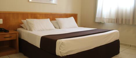 Cama bem arrumada com roupa de cama branca e marrom, cabeceira de madeira e um quadro na parede.