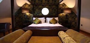 A bedroom with a large bed, two bedside lamps, patterned wallpaper, and a circular window. - Bears Paw Inn (Sandbach)