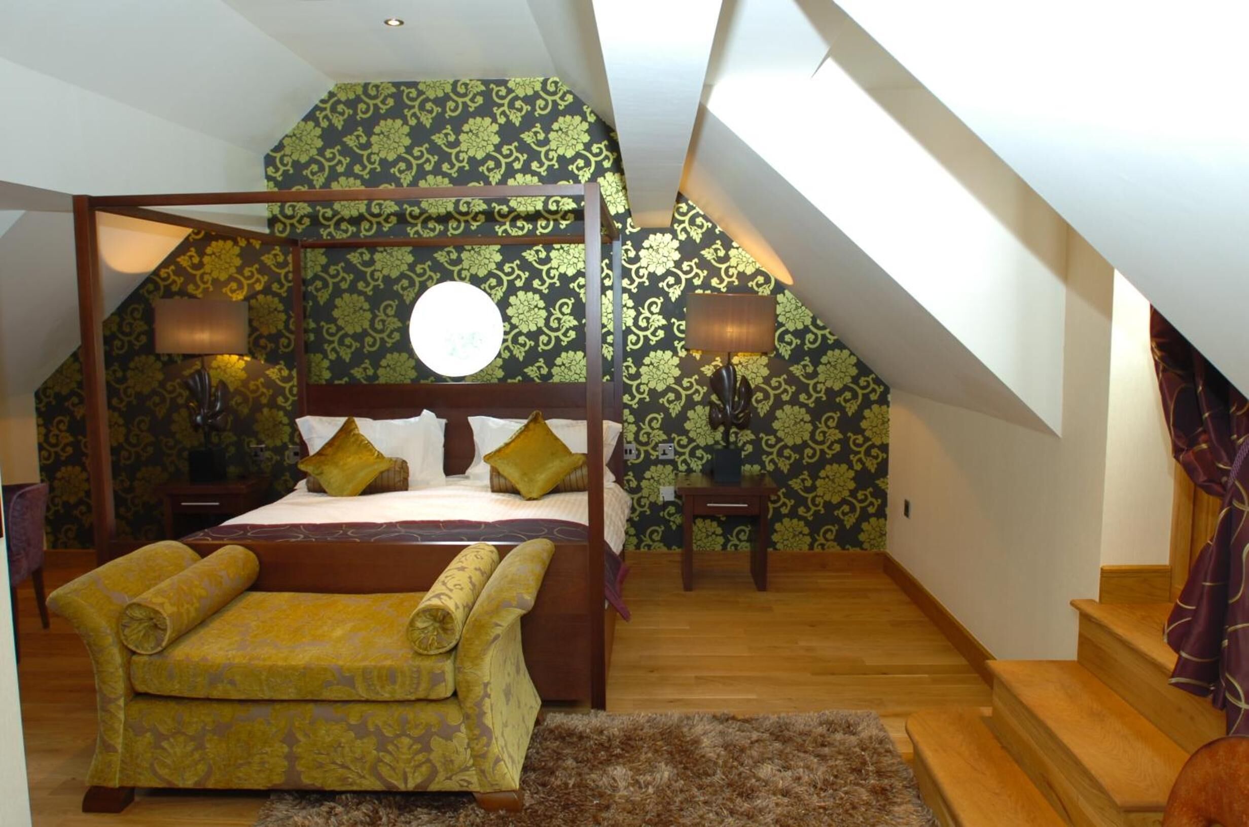 A bedroom with a four-poster bed, a sofa, two nightstands, and a staircase.