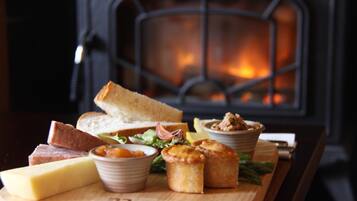 A wooden board with cheese, bread, and small baked goods in front of a fireplace.