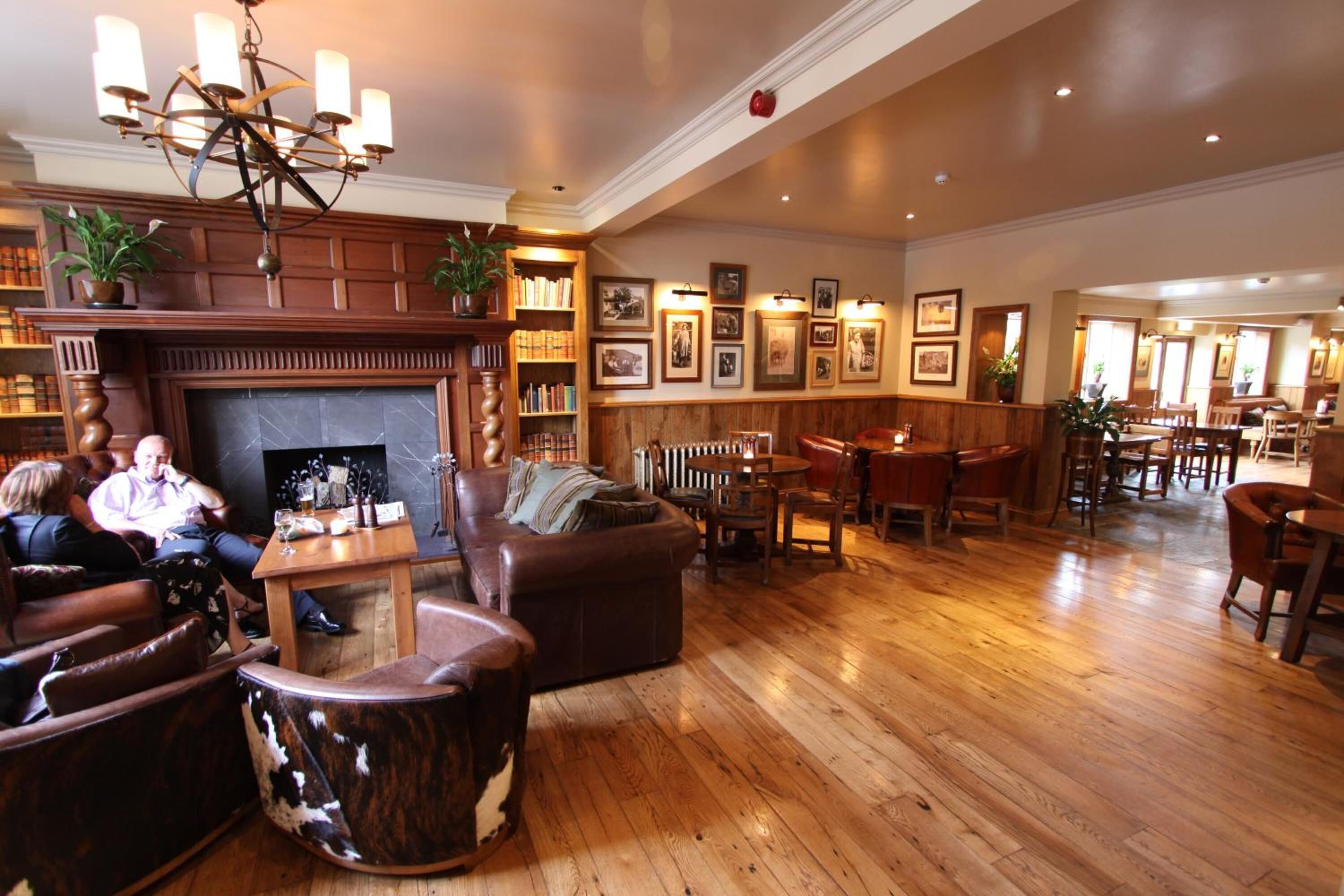 A spacious lobby with a fireplace, wooden flooring, leather seating, and a variety of framed pictures on the walls.