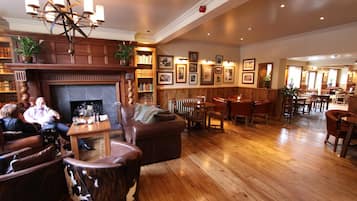 A spacious lobby with a fireplace, wooden flooring, leather seating, and a variety of framed pictures on the walls.