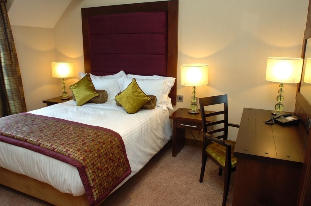 Una habitación de hotel con una cama grande, dos mesitas de noche con lámparas, un escritorio y una silla.