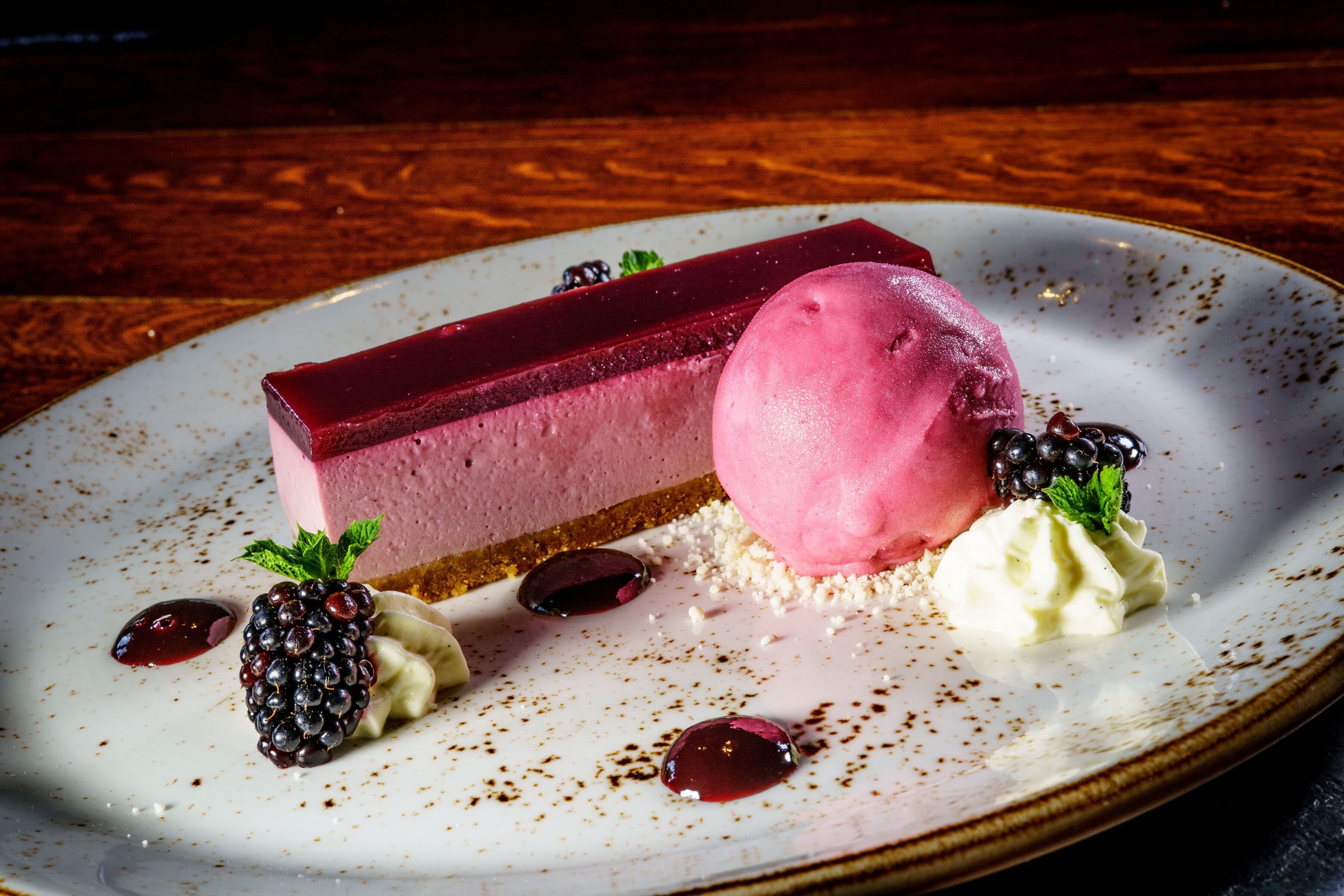 Ein Dessertteller mit einem Stück Käsekuchen, einer Kugel Eis und Beeren sowie Schlagsahne.