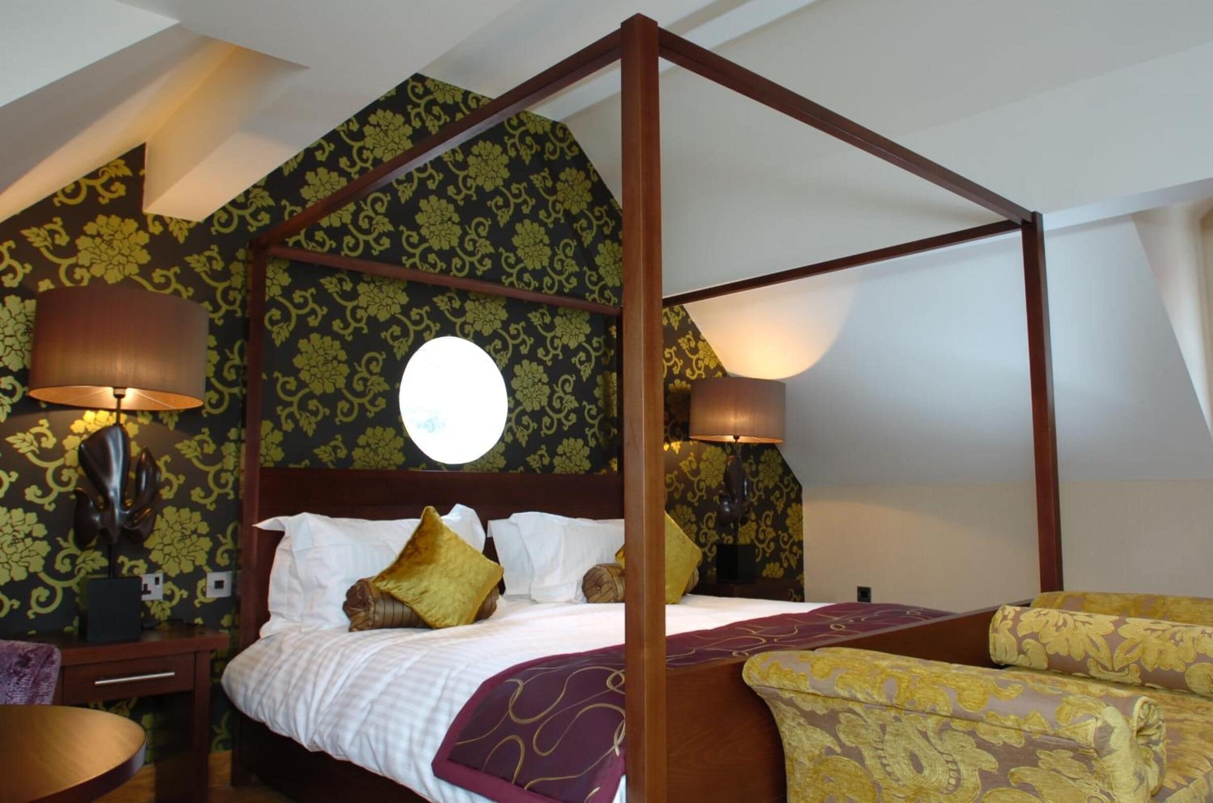 A four-poster bed with a canopy, two bedside lamps, and patterned wallpaper.