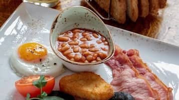 Prato de café da manhã com ovos, bacon, linguiça, cogumelos, feijão, torradas e um copo de suco de laranja.