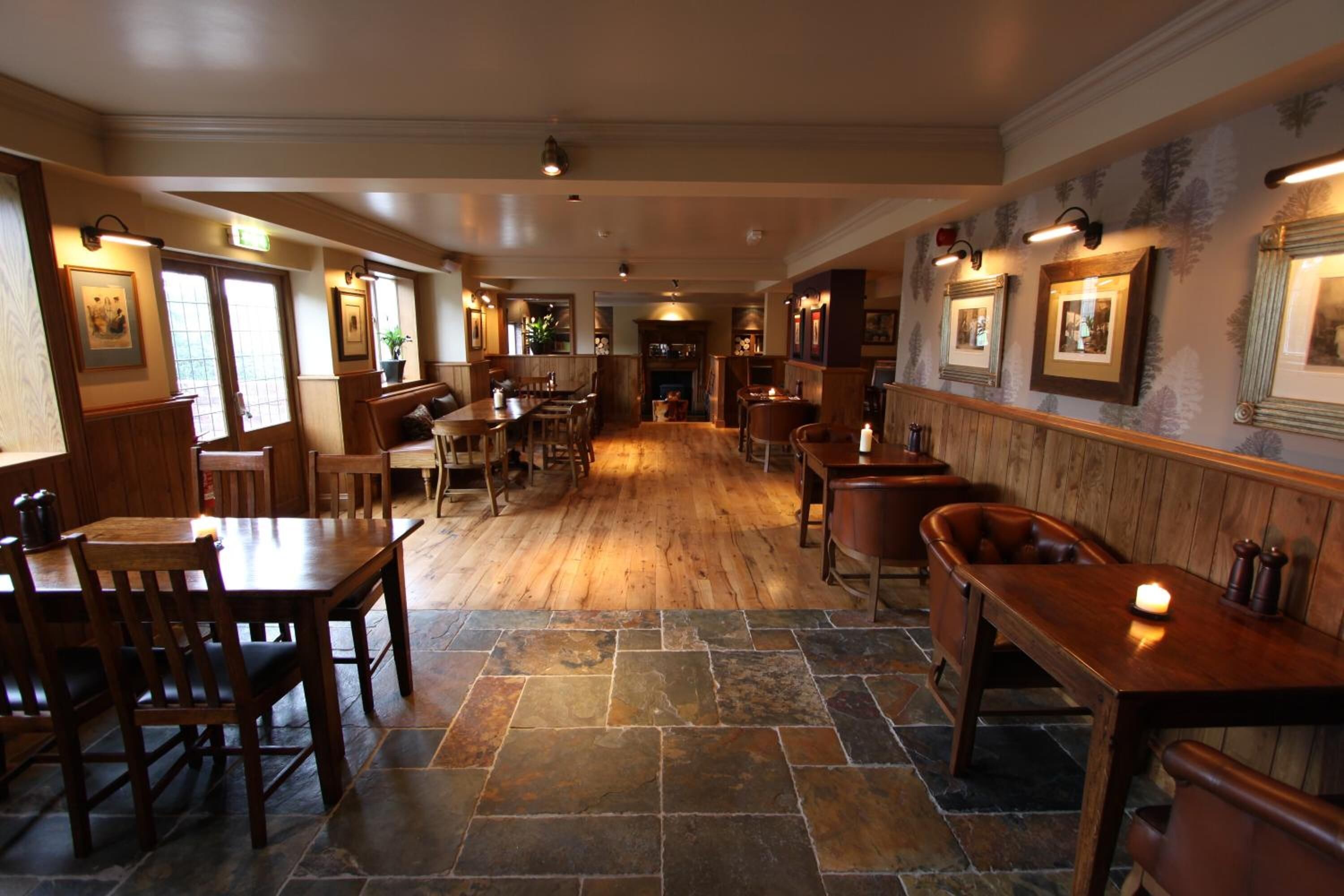 A spacious restaurant with wooden tables and chairs, stone flooring, and framed pictures on the walls.