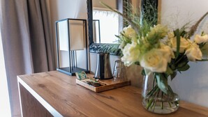 Een houten tafel met een theeschaal, een glazen vaas met witte bloemen, een kaars en een lijst met een spiegel.