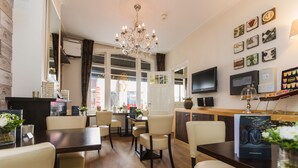 Een restaurantruimte in een hotel, met een kroonluchter, eettafels, stoelen, een televisie en decoratieve muurkunst.