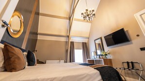 Een hotelkamer met een bed, een bureau, een stoel, een televisie, een spiegel en een kroonluchter.