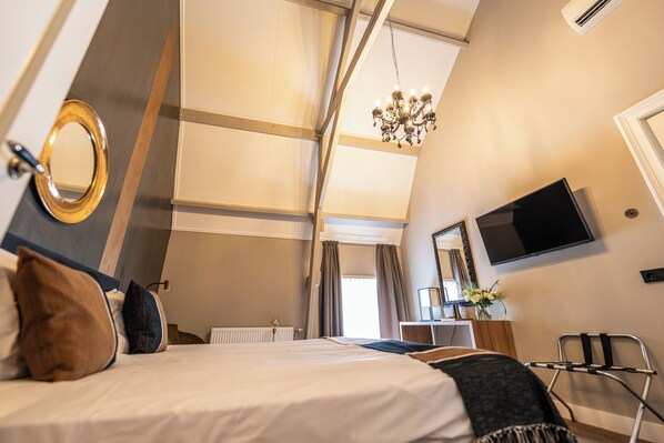 A hotel room with a bed, a desk, a chair, a TV, a mirror, and a chandelier. - Montfoort (Montfoort)