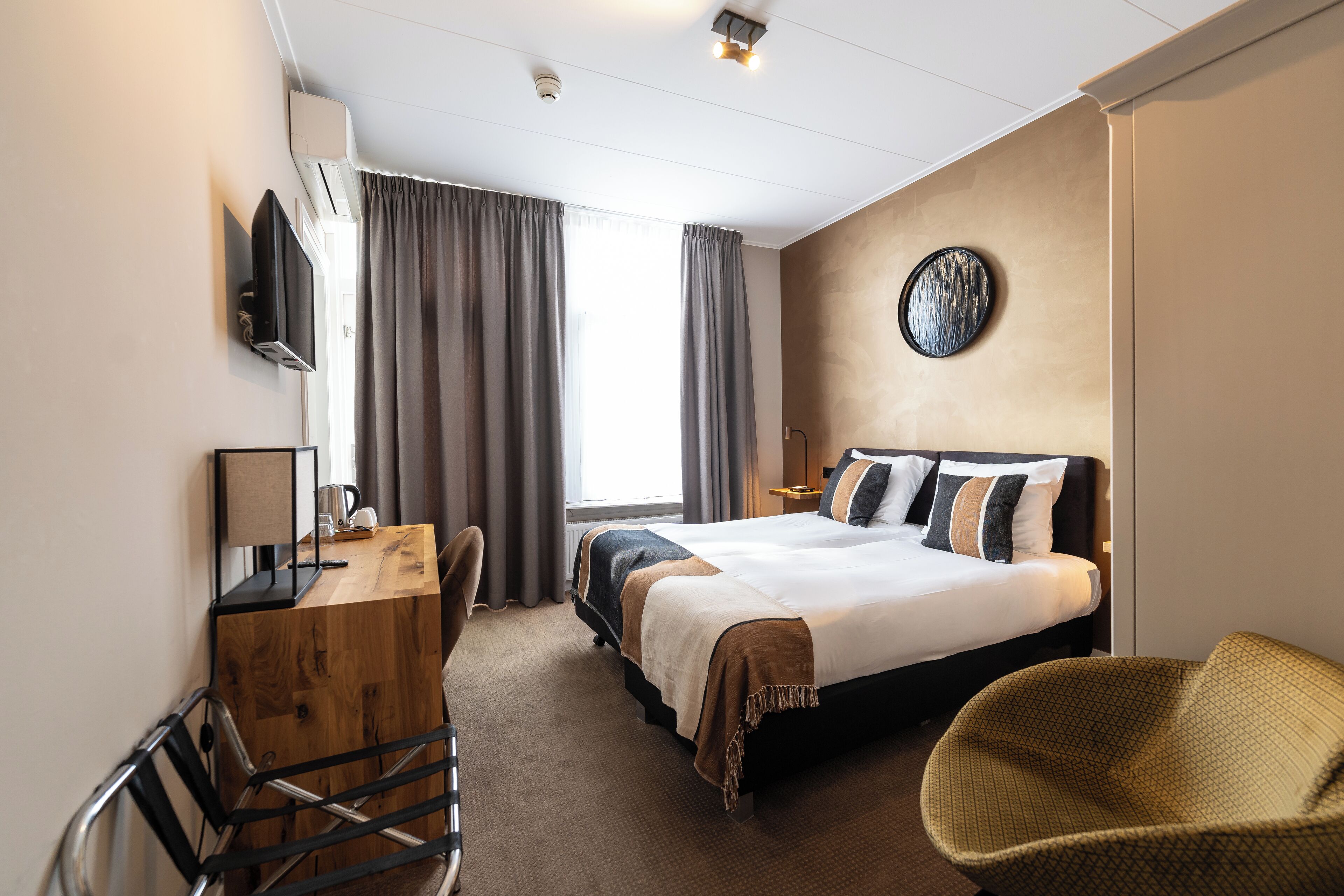 A hotel room with a bed, a desk, a chair, a TV, and a window with curtains.