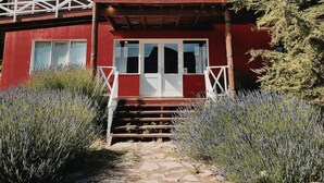 Un edificio de madera de dos pisos con fachada roja, ventanas de marco blanco y un nivel superior cubierto.