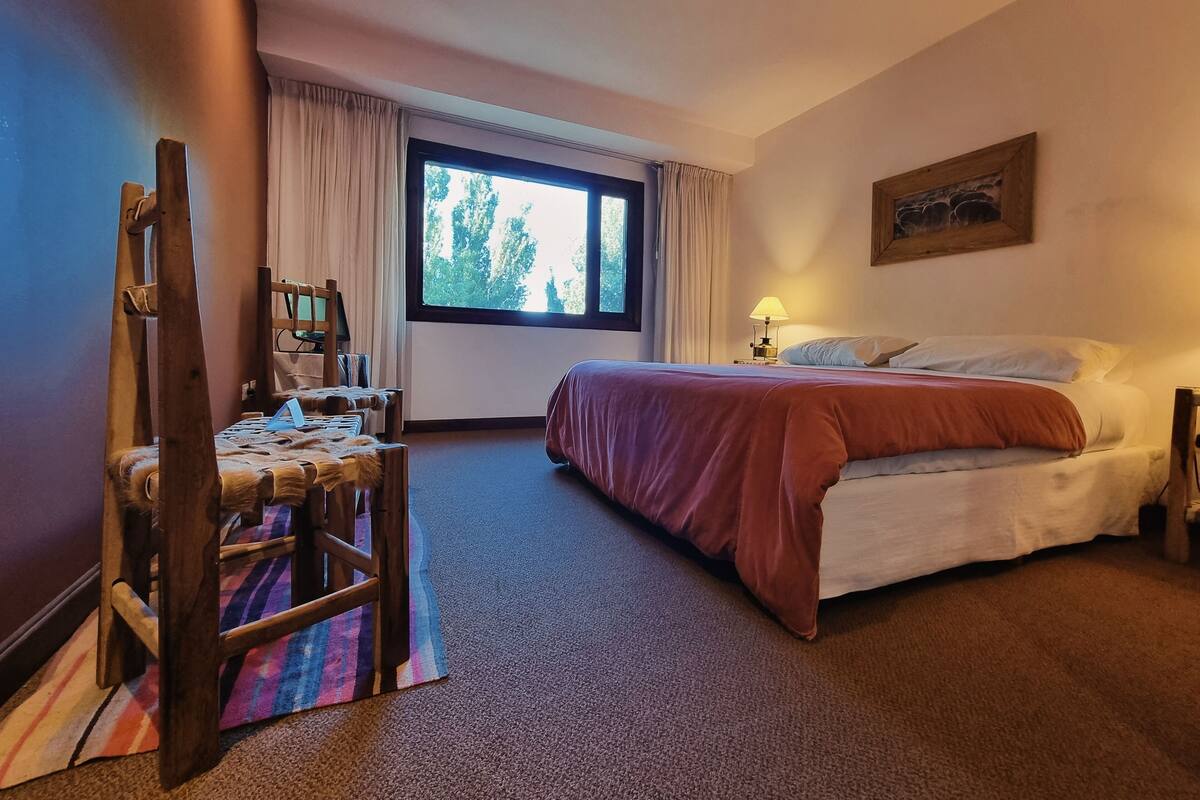 Une chambre d’hôtel avec un lit, un bureau et une chaise, une fenêtre avec des rideaux et une lampe.