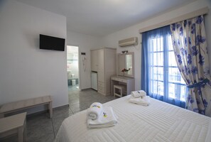 A hotel room with a bed, a desk, a vanity, and a television on the wall. - Hotel Ilion (Naxos)