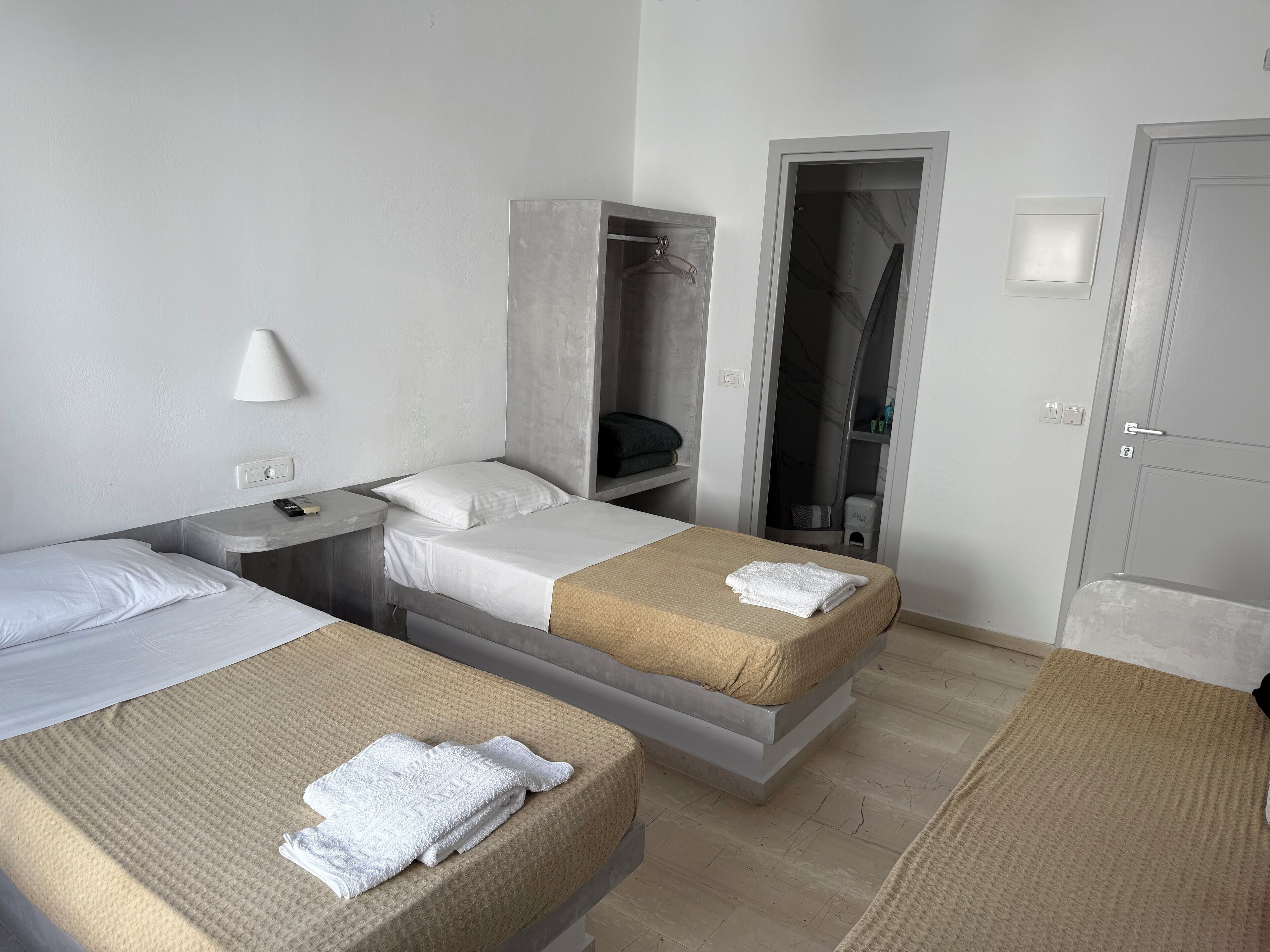 A hotel room with two beds, a wardrobe, a shower area, and a door.