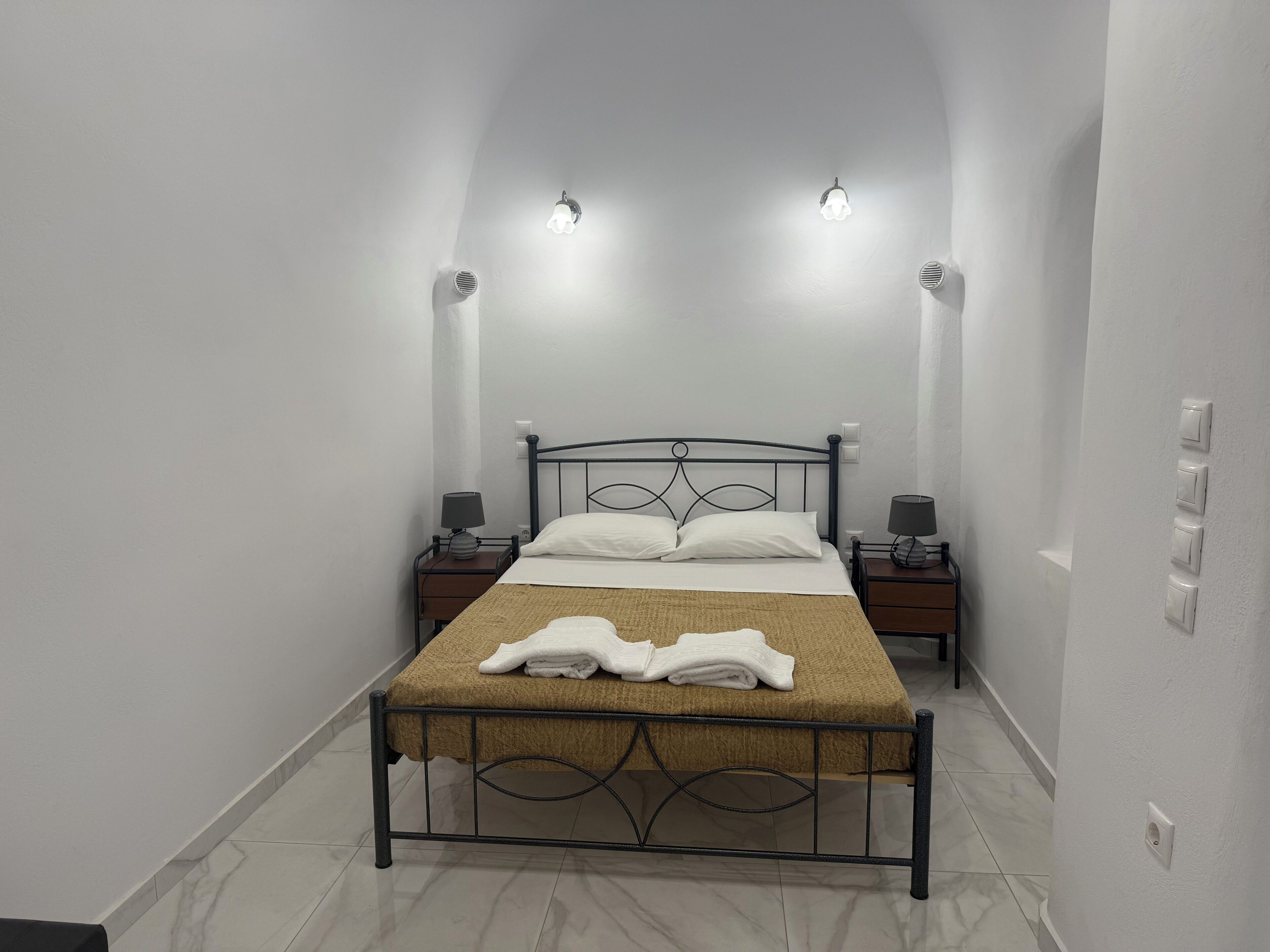 A narrow room with a single bed, two bedside tables, and wall-mounted lights.
