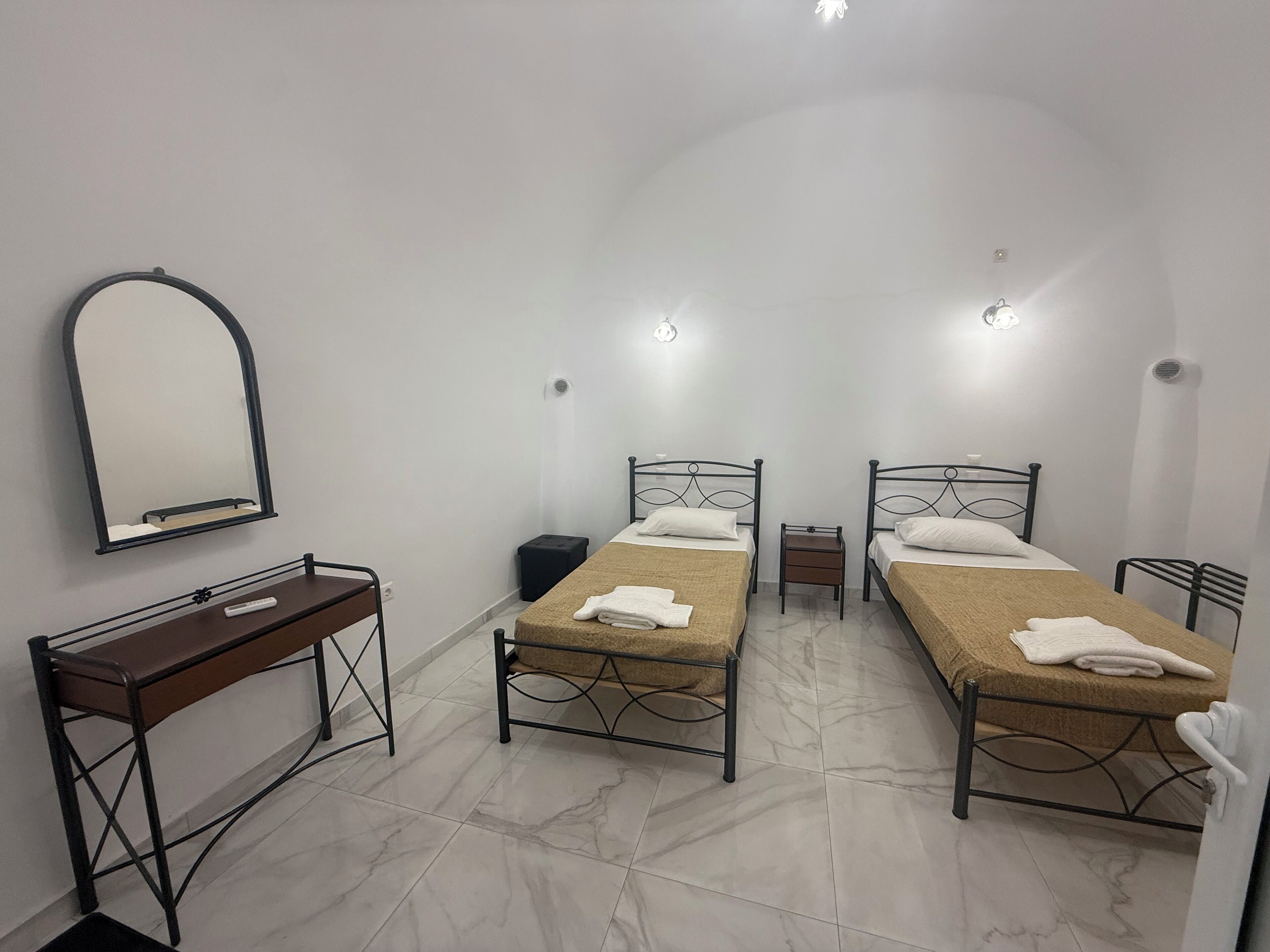 A room with two single beds, a small bedside table, a mirror, and a desk with a chair.
