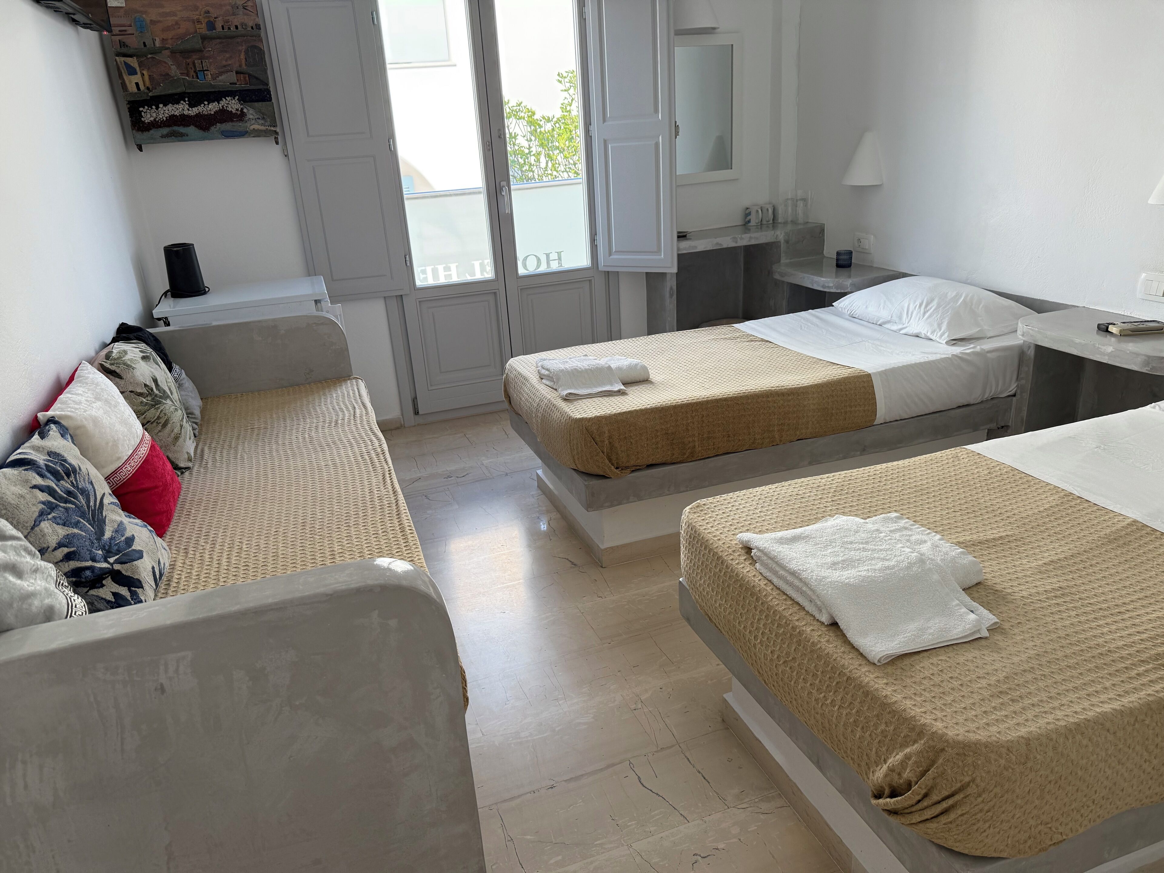 A hotel room with two beds, a sofa, a small table, and a mirror.