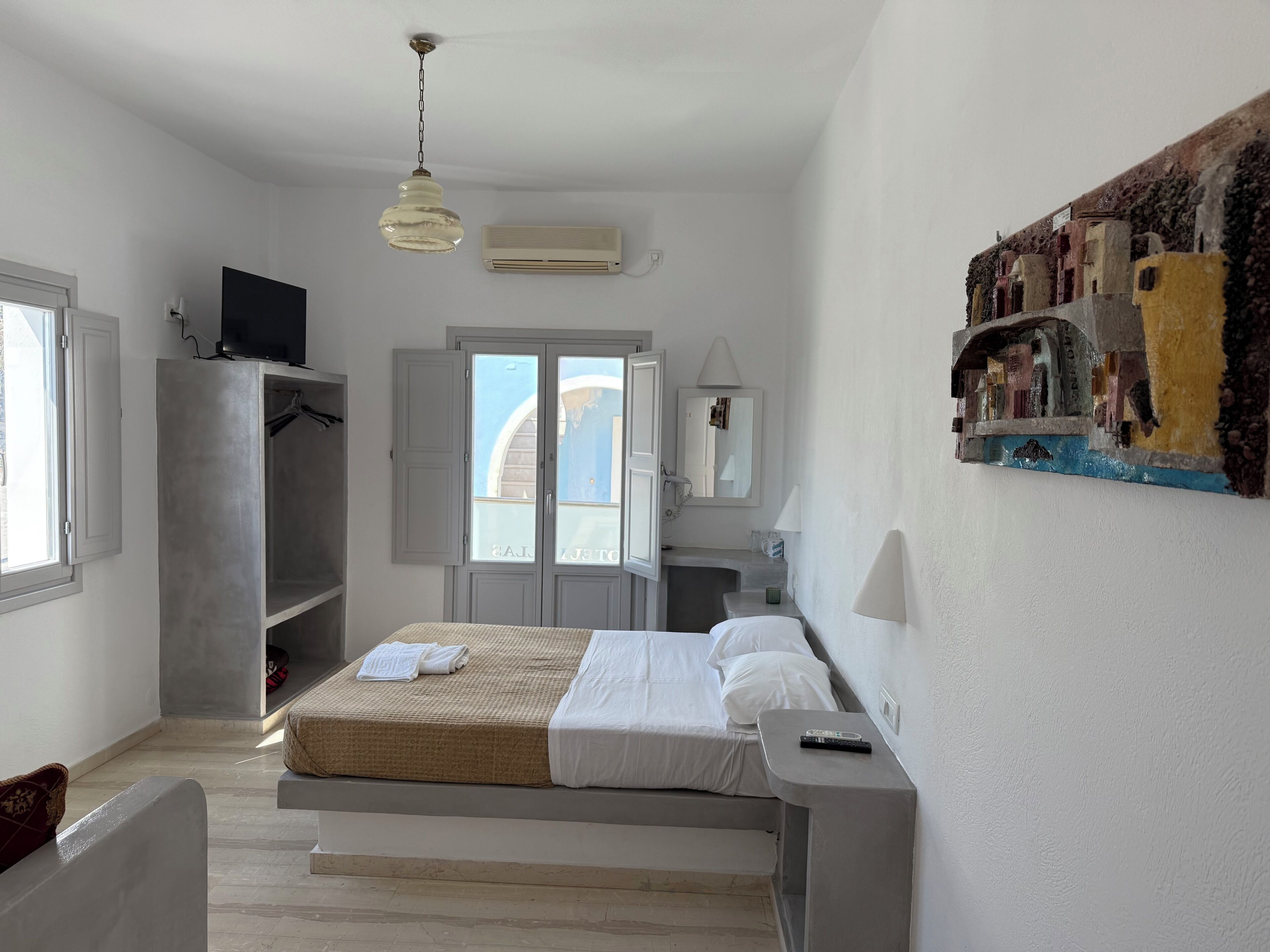 A bedroom with a bed, a TV, a wardrobe, and a bathroom with a mirror and sink.